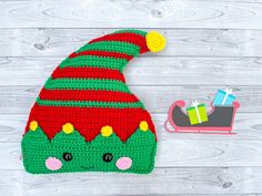 a crocheted christmas hat next to a toy sleigh on a white wooden background