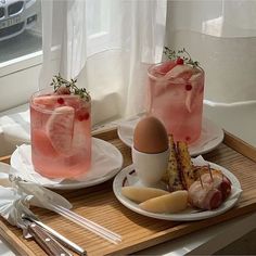 two drinks are sitting on plates next to each other in front of a window, with silverware and utensils