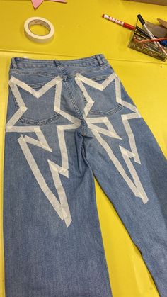 a pair of blue jeans with white lightning design on them, sitting next to scissors and pencils