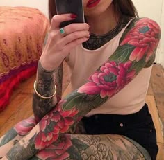 a woman sitting on the floor with her arm covered in tattoos and holding a cell phone