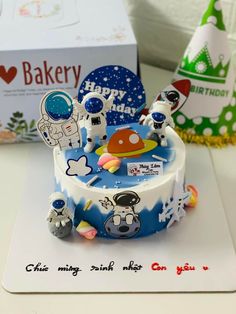 a birthday cake with an astronaut theme on it's side and a box in the background