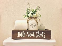 a wooden sign that says hello sweet cheeks on top of a toilet with soap and flowers