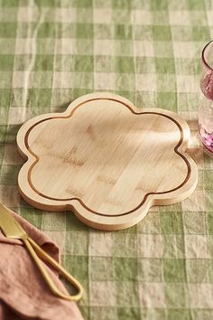 an empty wooden plate next to a glass and utensils on a green checkered tablecloth