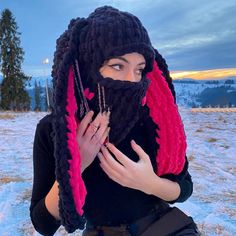 a woman with dreadlocks is sitting in the snow wearing a black and pink scarf