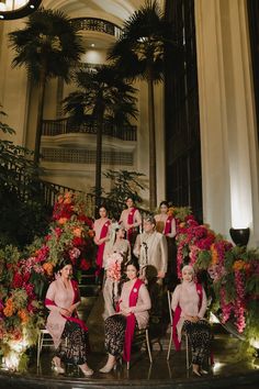 a group of women sitting next to each other on chairs in front of plants and flowers