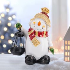 a snowman figurine with a lantern and christmas tree in the background