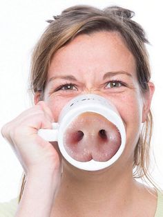 a woman holding a coffee cup in front of her nose and making a funny face