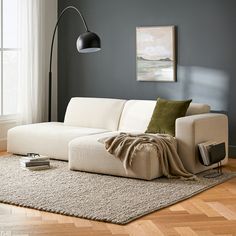 a white couch sitting on top of a wooden floor in a living room next to a window