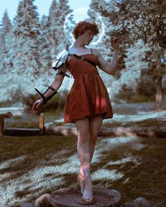 a woman in an orange dress standing on top of a tree stump with her arm outstretched