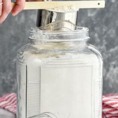 a person is using a wooden spoon to mix ingredients in a mason jar on a red and white checkered cloth