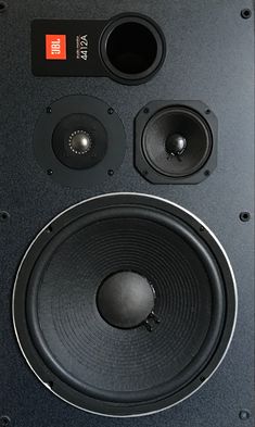 two speakers sitting on top of each other in front of a black wall mounted speaker