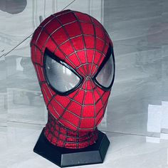 a spider - man mask is sitting on top of a black stand with white walls behind it