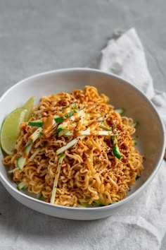 a white bowl filled with noodles and garnished with green onions, lime wedges and shredded cheese