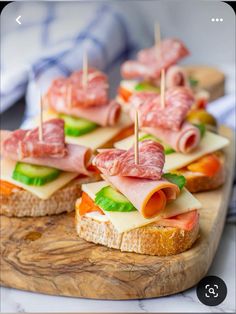 small sandwiches with meats and cheese are on a cutting board, ready to be served