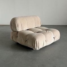 a beige couch sitting on top of a cement floor next to a white wall in an empty room