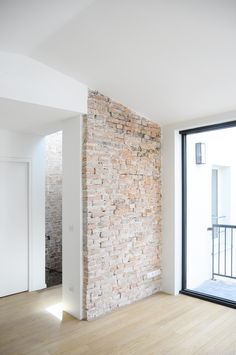 an empty room with wooden floors and a brick wall on one side, looking out onto the street