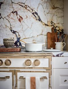 a white stove top oven sitting inside of a kitchen next to a wall covered in marble