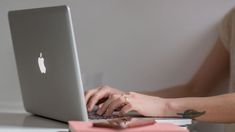 a woman sitting at a desk using a laptop computer with her hand on the keyboard