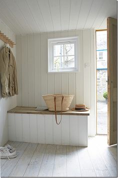 a wooden bench sitting in the middle of a room next to a window and coat rack