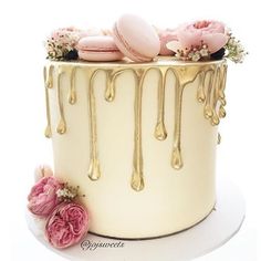 a white cake with gold icing and pink macaroons on the top layer