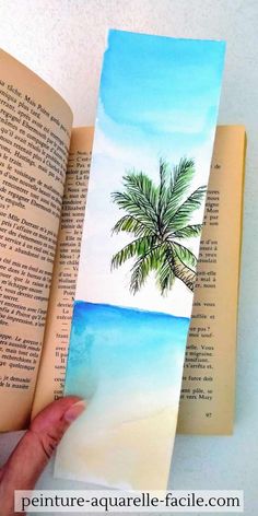 an open book with a painting of a palm tree on the beach next to it