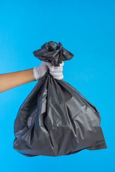 a hand holding a black trash bag on a blue background