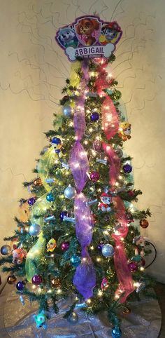 a brightly colored christmas tree with lights and decorations on it's base, in front of a wall