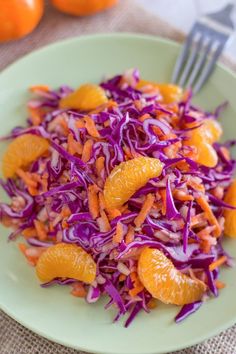 a salad with oranges and cabbage on a green plate next to silver utensils