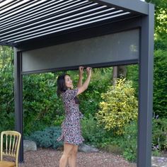 a woman in a dress reaching up into the air with her hand on top of a pergolated structure