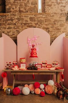 a table topped with lots of cakes and desserts next to a wall covered in pink walls