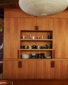 a wooden cabinet with plates and cups on it's shelves next to a potted plant