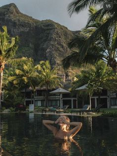 a woman laying on the edge of a pool in front of palm trees and mountains