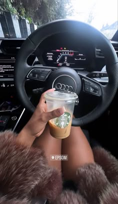 a woman is holding a starbucks cup in her hand while sitting in the driver's seat of a car