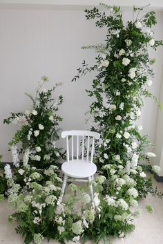 a white chair sitting in front of a bunch of flowers and greenery on the floor