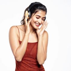 a woman with headphones on smiling and holding her hands to her face while standing in front of a white background