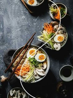 two bowls filled with vegetables and hard boiled eggs on top of a black surface next to chopsticks