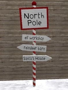 a pole that has signs on it in front of a wooden building and snow covered ground