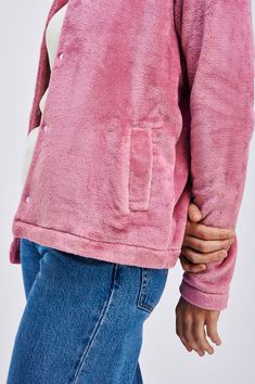 a person wearing a pink jacket and jeans with their hands on the back of their stomach