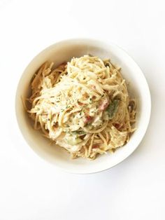 a white bowl filled with pasta and sauce on top of a white countertop next to a fork