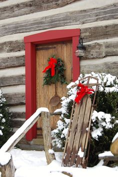 a wooden sled sitting in front of a red door with wreaths on it