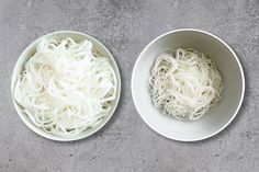 two white bowls filled with noodles on top of a gray table next to each other