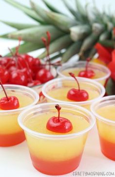 small cups filled with liquid and topped with cherries on a table next to pineapples