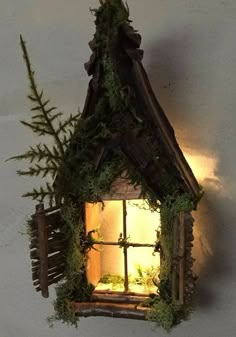 a small house made out of wood and plants is lit up by a light that shines in the window