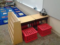 two red crates sitting on top of a wooden table next to a white board with writing on it