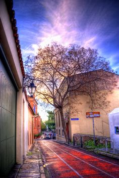 an empty street with trees and buildings on both sides, under a cloudy blue sky