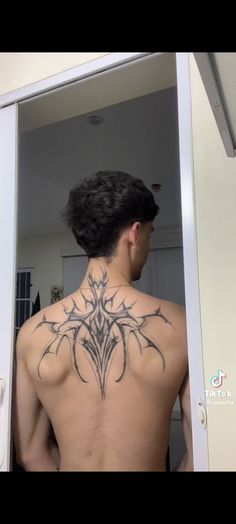 a man with a tattoo on his back standing in front of a mirror looking at himself