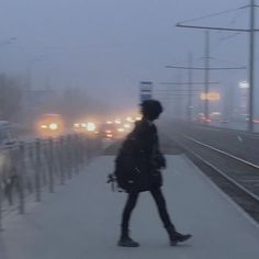 a person walking down a sidewalk next to a street filled with traffic on a foggy day