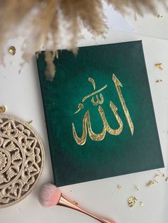 a green and gold greeting card with arabic writing on it next to a brush in front of some confetti