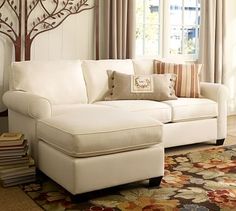 a living room with a large white couch and pillows on the floor next to a window