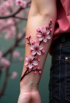 a woman's arm with pink flowers on it and a tree branch in the background